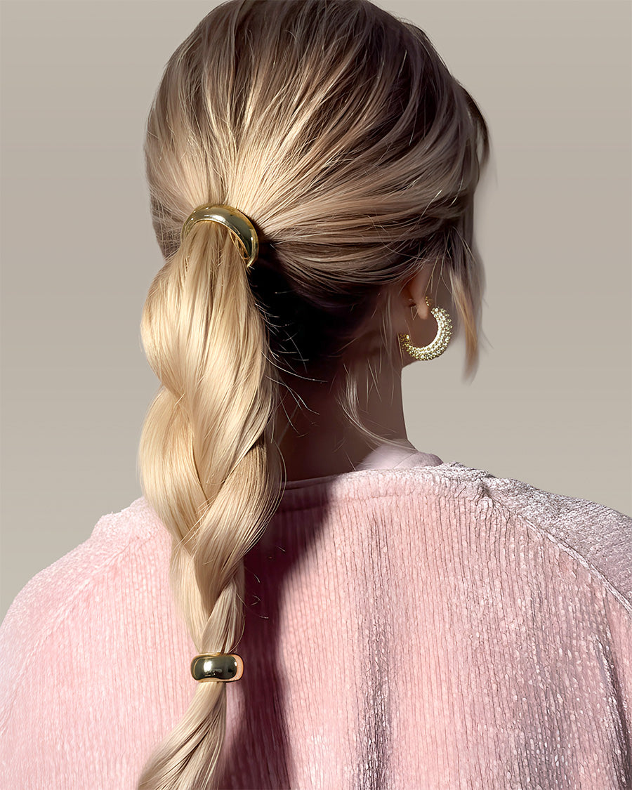 KELA Ponytail Halo Hair Clip Ponytail Holder in gold plated metal securing a blonde braided ponytail on a woman wearing a pink textured top